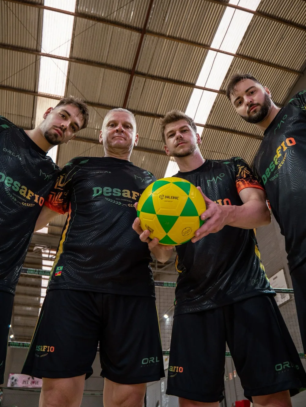 Quarteto masculino de futevôlei com uniforme preto e detalhes em verde e laranja